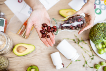 Holding dried rose hips at the table with healthy vegan food ingredients and supplements, top view. Concept of rose hips as a new trend in food and cosmetic industry