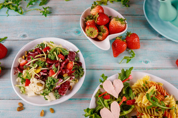 Italian pasta salad with heart sausage and salad on wooden table.
