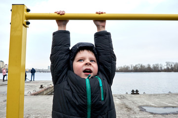 Fototapeta premium Little boy hanging on the horizontal bar in winter.