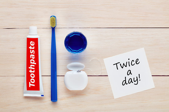 Toothbrush, toothpaste, dental floss and mouthwash with a twice a day note on wooden table