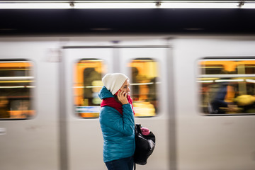 Woman standing in subway station and talking on the phone. Subway train is passing in blurred motion