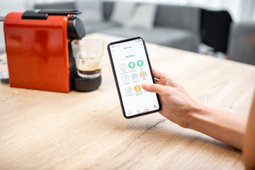 Modern coffee machine connected online with smartphone application. Concept of a smart home and mobile application for managing devices at home