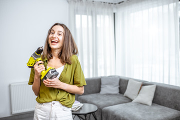 Portrait of a young and happy handywoman with cordless screwdriver at home. Concept of an easy household work with modern working tools