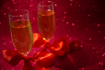 Two glasses of champagne decorated red ribbon on red glittering background. Valentines day or Wedding celebration concept. Copy space. Soft focus
