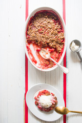 Crunchy strawberries crumble, top view, served with vanilla ice cream, on an oval serving dish, ,...