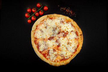 Isolated round pizza on black background with tomatoes