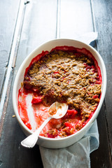 Crunchy strawberries crumble, top view, halfserved, on an oval serving dish,on a rustic wooden  background