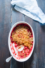 Crunchy strawberries crumble, top view, halfserved, on an oval serving dish,on a rustic wooden  background