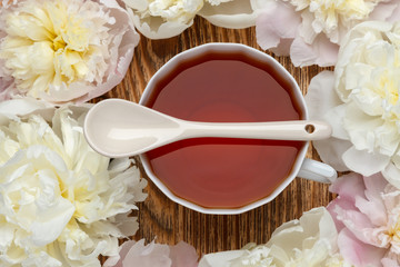 Flat lay over wooden background with peonies, cup of tea and  ceramic spoon