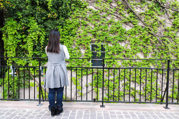 Young Asian woman standing in front of building which covered by overgrow creeper plant. She...