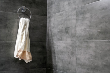 A light terry towel hangs on a chromed ring holder on a gray concrete wall in the corner of a modern bathroom