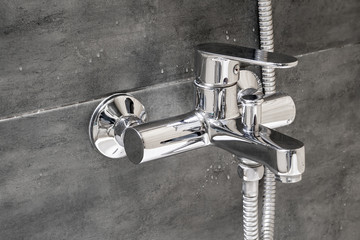 Chrome metal faucet for hot and cold water, with a shower hose, mounted in a wall covered with gray...