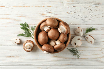 Champignon mushrooms in bowl and dill on wooden background, top view