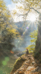 Sunshining in autumn forest. Girl sits on the cliff edge. Sochi, Russia.