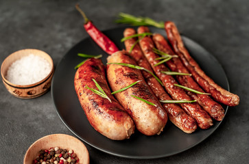 different grilled sausages in a dark plate with spices and rosemary, on a stone table, ready to eat with copy space for your text