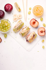 Fruit spring rolls in rice paper next to ingredients with banana, apple, grape and plum on a white background. There is a place for the text Proper nutrition