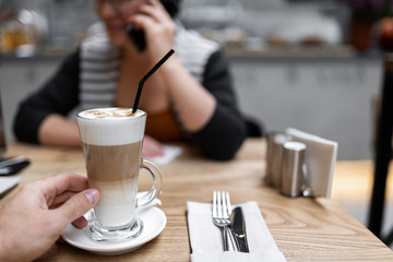 latte coffee in a man’s hand at the table on the background of a girl. Breakfast together.