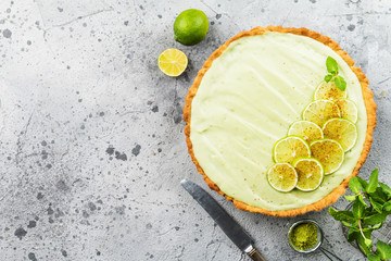 Key Lime Pie with several limes and mint over gray background, top view with copy space.