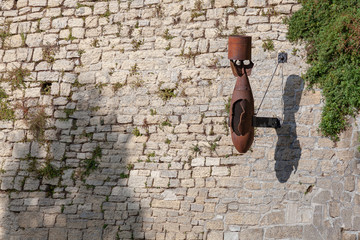 Background image - wall of an old fortress with a rusty aerial bomb attached to it