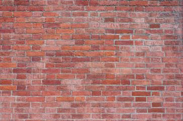 A fragment of the exterior wall of a red brick building. Bricks have different shades and surface texture. Background.