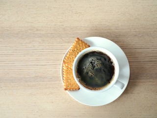 Picture seen from the top of hot black coffee in a white ceramic mug served with small pieces of bread.