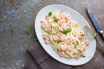 Italian pasta spaghetti in a creamy sauce with shrimp in a plate, top view