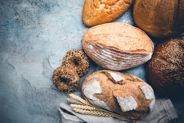 Assortment of fresh baked bread and buns on stone background, top view