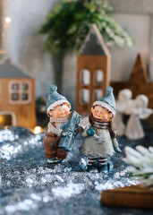 Porcelain figurines of children in a Christmas decor. Winter figurines of a boy and a girl with gifts on the background of houses and cones. Christmas Greeting Card. Copy space.