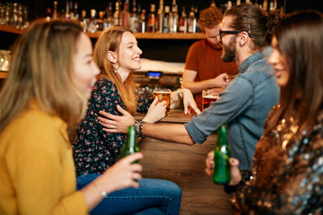 Group of friends drinking beer, chatting and talking to barman. Night out. Pub interior.