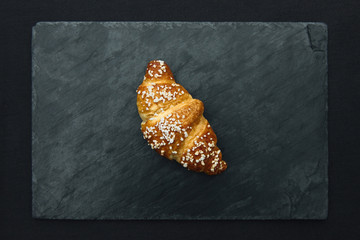 Fresh croissant on a black slate background.