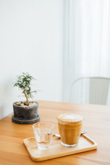 cup of latte coffee and water in glass with tree pot on wooden table