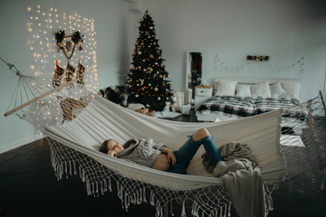 Pregnant woman sleeps in hammock against background of Christmas decorations.