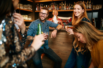 Group of friends drinking beer, chatting and talking to barman. Night out. Pub interior.