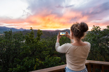 Young girl woman taking picture with phone of view at Aspen, Colorado rocky mountains colorful sunset in background - Powered by Adobe