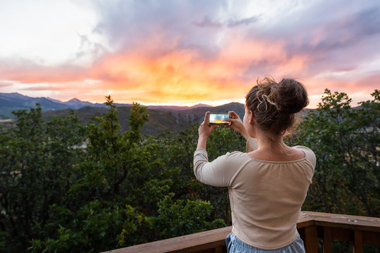 Young girl woman taking picture with phone of view at Aspen, Colorado rocky mountains colorful sunset in background