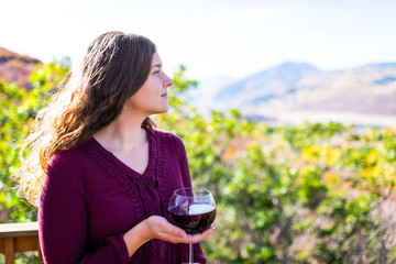 Woman holding red wine glass on terrace railing and bokeh background view of autumn foliage yellow...