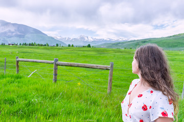 Fototapeta na wymiar Crested Butte, Colorado view in summer in Rocky Mountains with young woman girl looking at meadow field farm and fence