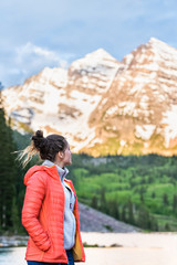 Maroon Bells in Aspen, Colorado in 2019 summer at sunrise with young girl woman in coat looking at peak view by lake