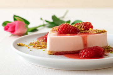 White wooden table with mini cheescake dessert embellished with real raspberries, raspberry syrup and cruhed pistachio nuts and rose flower.