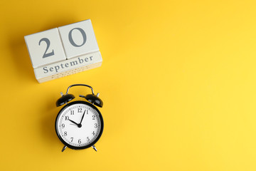 Wooden block calendar and alarm clock on yellow background, flat lay. Space for text