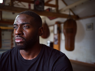 Male Boxer In Gym Standing By Old Fashioned Leather Punch Bag