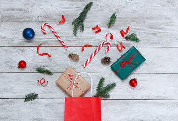 Christmas baubles, gifts, candy canes, cones, streamer, fir tree branch. Explosion from shopping bag on white wooden table. Christmas background concept. New Year, sale, copy space, top view