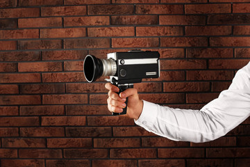 Man with vintage video camera near brick wall, closeup of hand