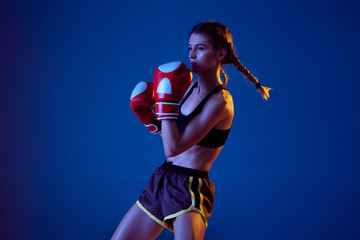 Activity. Fit caucasian woman in sportswear boxing on blue studio background in neon light. Novice female caucasian boxer working out and training. Sport, healthy lifestyle, movement concept.