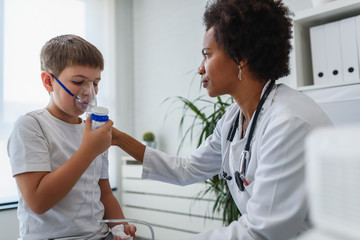 Woman African American doctor general practitioner helping child to put nebulizer inhaler face mask. Asthma treatment for children. - obrazy, fototapety, plakaty