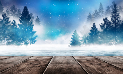 Winter background. Winter snow landscape with wooden table in front. Dark winter forest background at night. Snow, fog, moonlight. Dark neon night background in the forest with moonlight. 