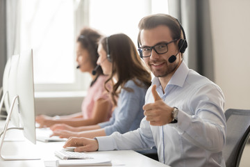 Smiling male employee in headset show thumb up