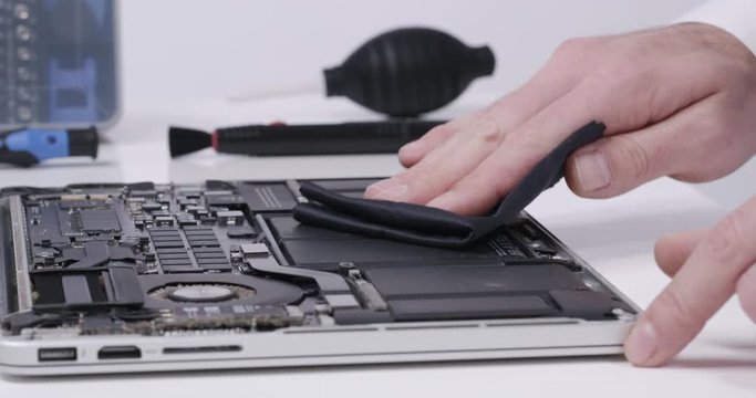 Service worker repairing cleaning dust laptop motherboard circuit board cooler with microfibre cloth in white walled lab in 4k
