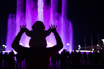 man with a child on his neck holds hands silhouette against the backdrop of a night fantasy.