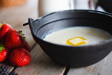 Traditional breakfast milk porridge with butter and berries on a wooden table.